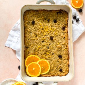 baked oats in a white baking dish with orange slices on a pink background