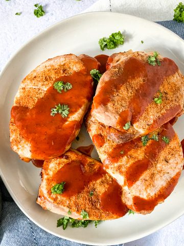 4 pork chops on a white dish with blue napkin