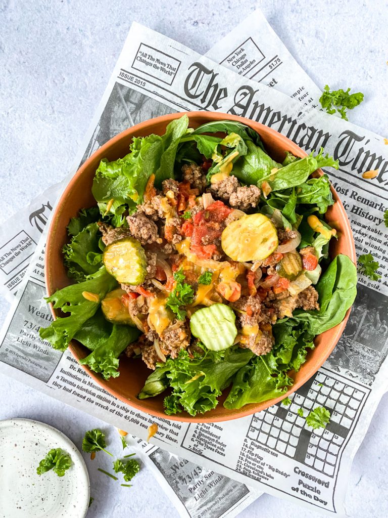 Bunless burger in a bowl of lettuce over newspaper