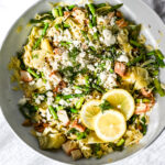 Bowl of lemon chicken orzo pasta with asparagus, artichoke hearts, crumbled feta cheese, fresh dill, and lemon slices