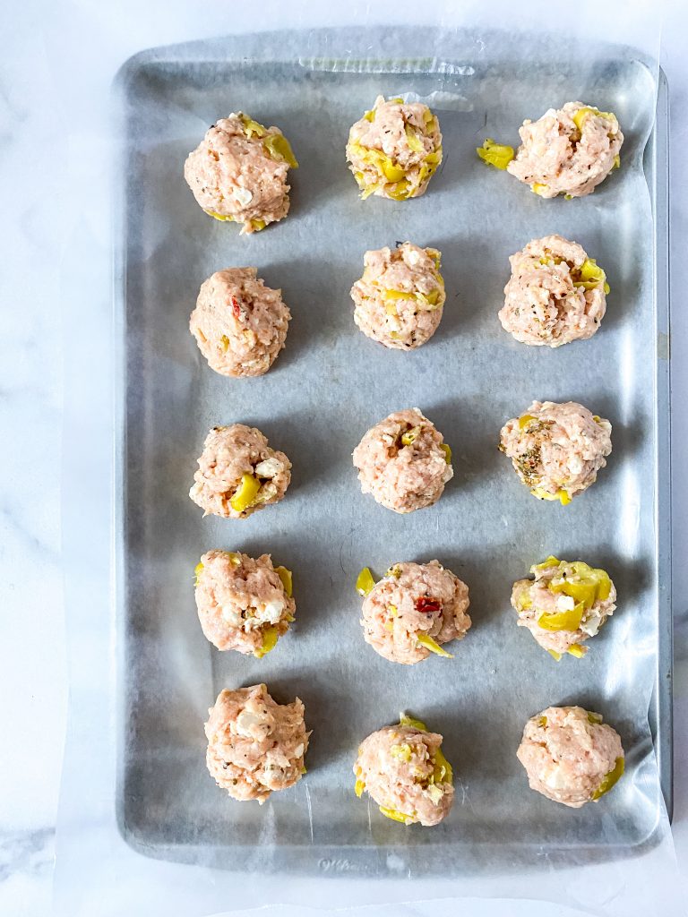 A sheet pan with parchment paper and greek meatballs lined up