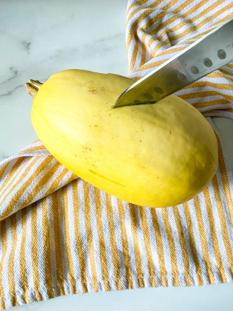 A spaghetti squash being pierced by a large knife on a yellow and white striped napkin