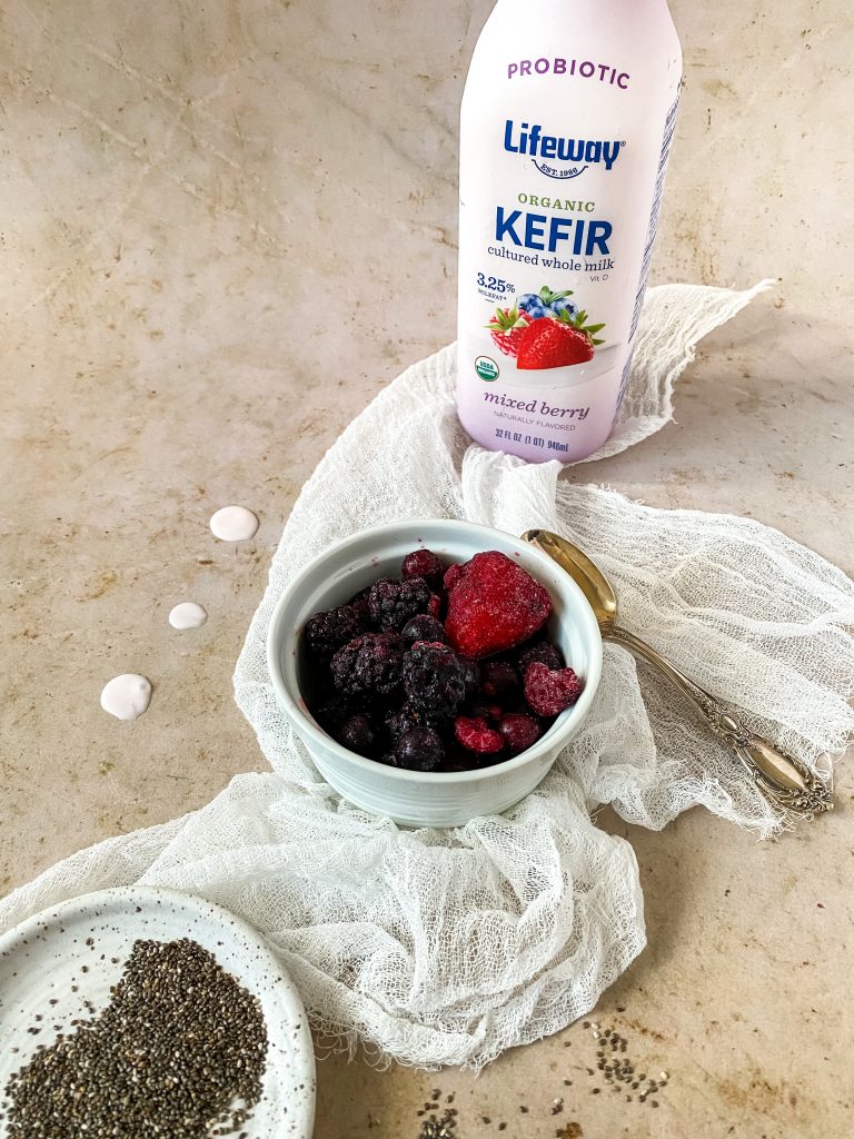 chia seeds and berries in separate bowls and berry kefir with a spoon on the side and a pink background