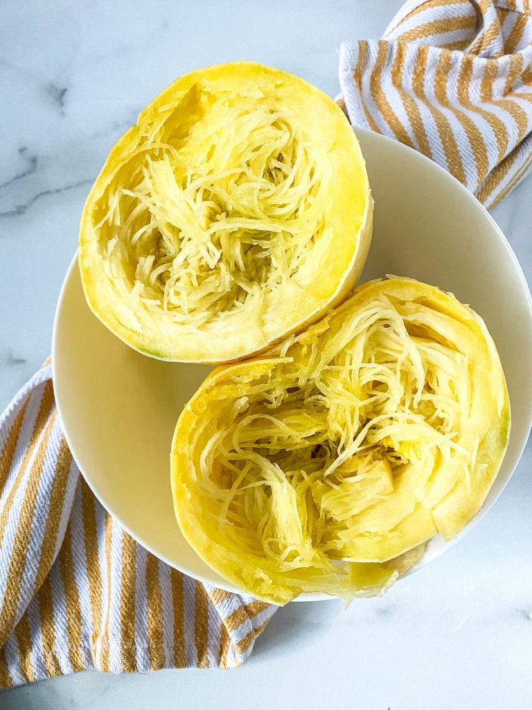 a cooked spaghetti squash cut in half in a white bowl on a yellow and white striped napkin