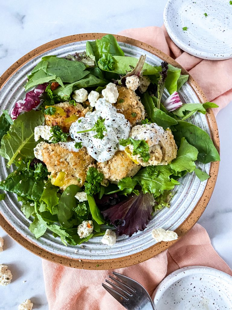 A bowl with spring mix and greek meatballs on a pink napkin