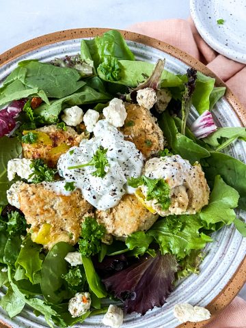 A bowl with spring mix and greek meatballs on a pink napkin