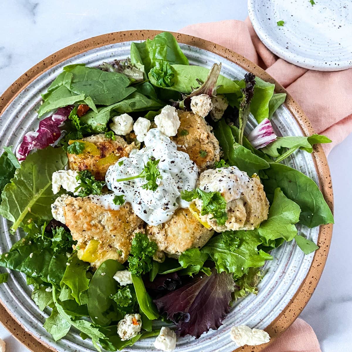 A bowl with spring mix and greek meatballs on a pink napkin