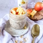 a small mason jar of oats with chopped apples and a cutting board in back