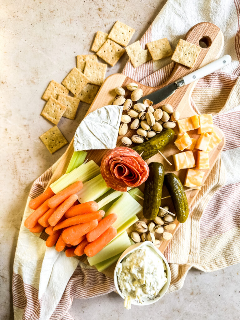 a small charcuterie board with vegetables, cheese, meat and crackers on the side