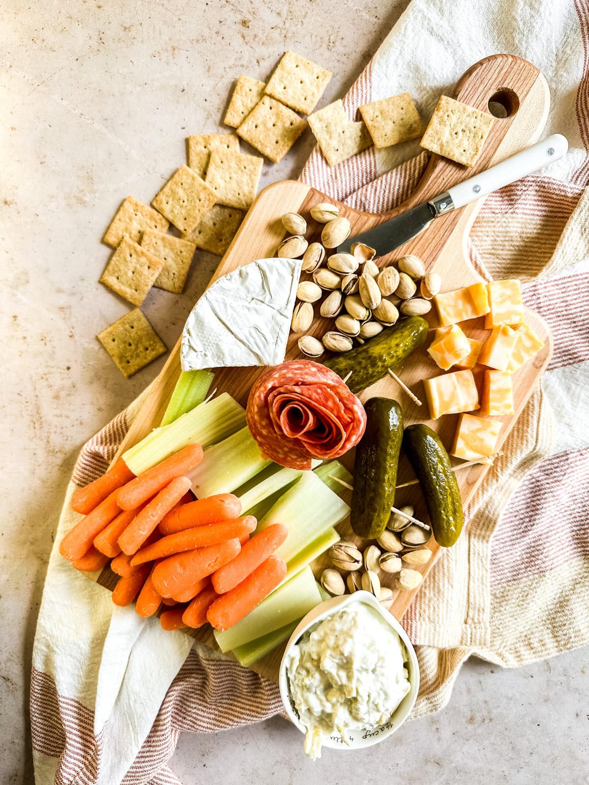 a small charcuterie board with vegetables, cheese, meat and crackers on the side