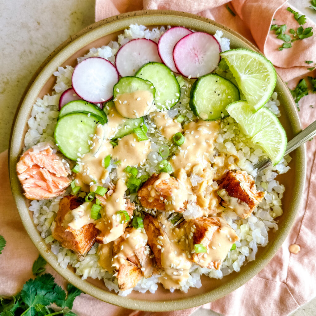a bowl with rice, salmon, cucumber, and radishes