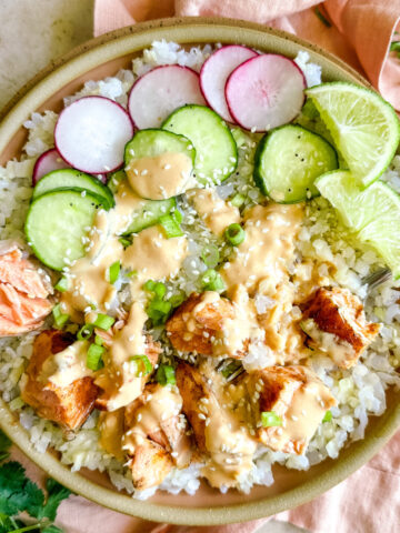 a bowl with rice, salmon, cucumber, and radishes