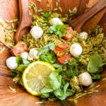 a bright orzo pasta salad being tossed in a wood bowl
