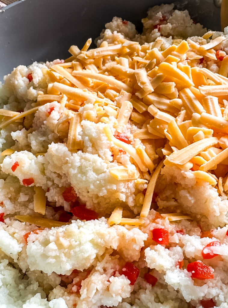 A bowl of grits with cheese and red peppers.