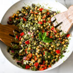 Close-up of chickpea quinoa salad with black beans, tomatoes, red onion, and fresh mint garnish served with wooden forks