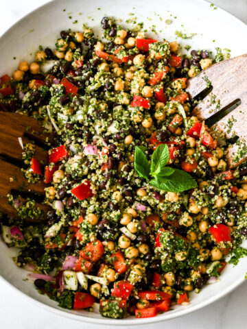 Close-up of chickpea quinoa salad with black beans, tomatoes, red onion, and fresh mint garnish served with wooden forks